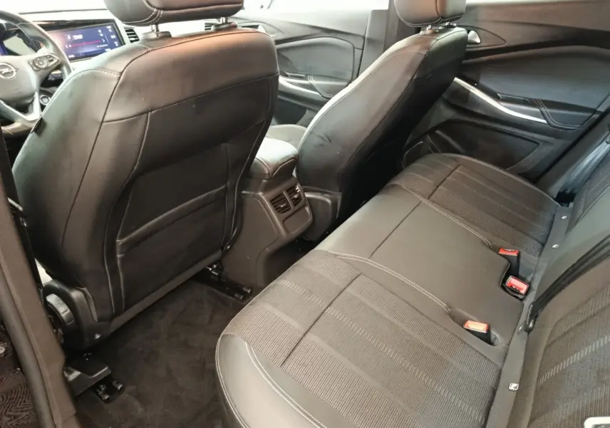 Vue intérieure arrière de l’Opel Grandland hybride 2023, sièges noirs en cuir et tissu avec console centrale et aérateurs.