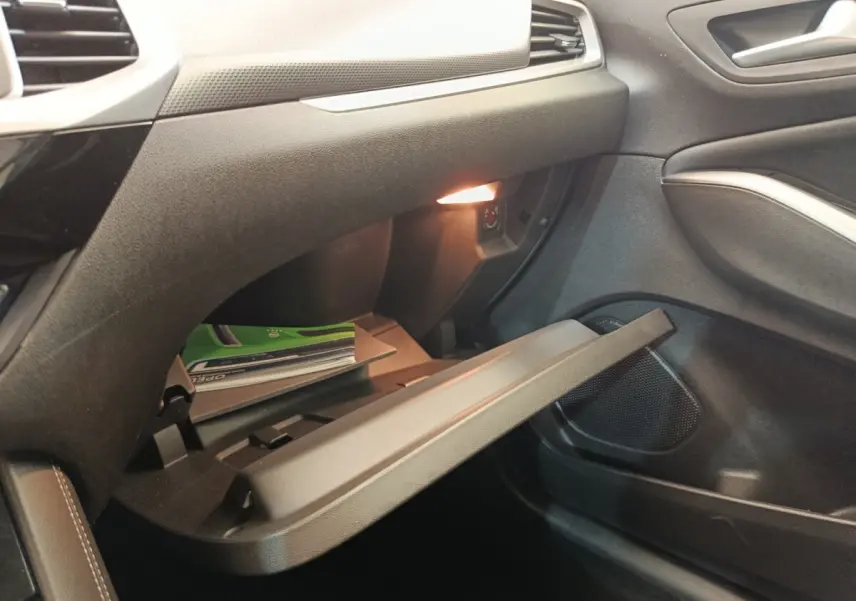 Gros plan de la boîte à gants ouverte côté passager de l’Opel Grandland hybride noire, avec éclairage intérieur allumé.