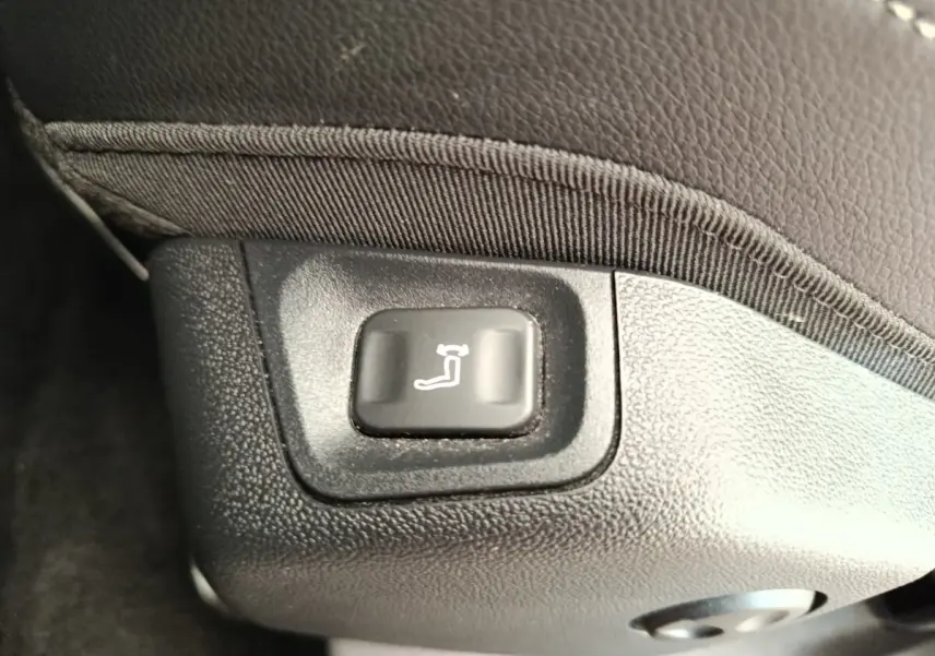 Bouton de réglage électrique de l'inclinaison du siège avant, sur revêtement noir texturé.