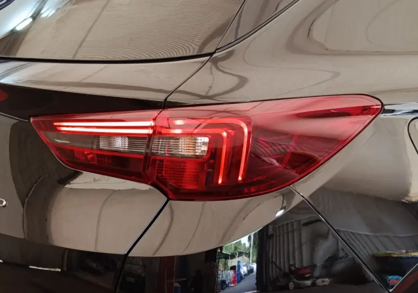 Gros plan sur le feu arrière droit rouge d’un Opel Grandland hybride rechargeable noir 2023, reflet d’atelier visible.