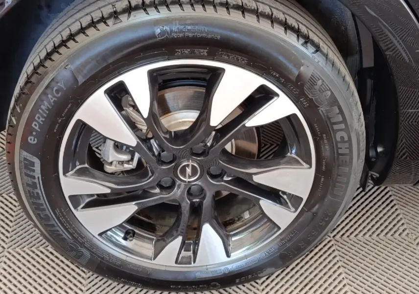 Gros plan sur la jante alliage bicolore noir et argent avec logo Opel, montée sur pneu Michelin d’un Opel Grandland noir.