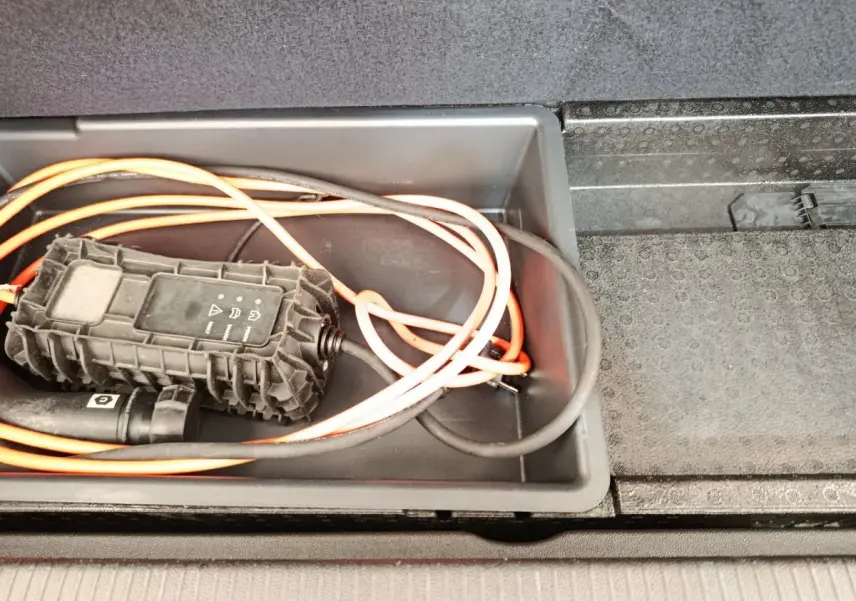 Gros plan sur le câble de charge orange et noir rangé dans le coffre du coffre d’un Opel Grandland hybride noir 2023.