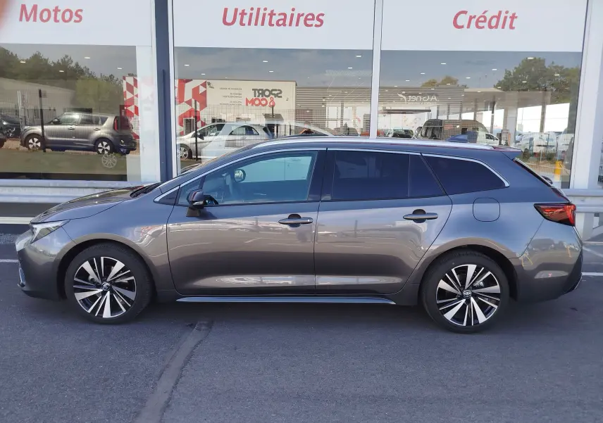 Profil latéral droit d'une Toyota Corolla Touring Sport gris atlas, avec jantes alliage bicolores et vitres teintées.