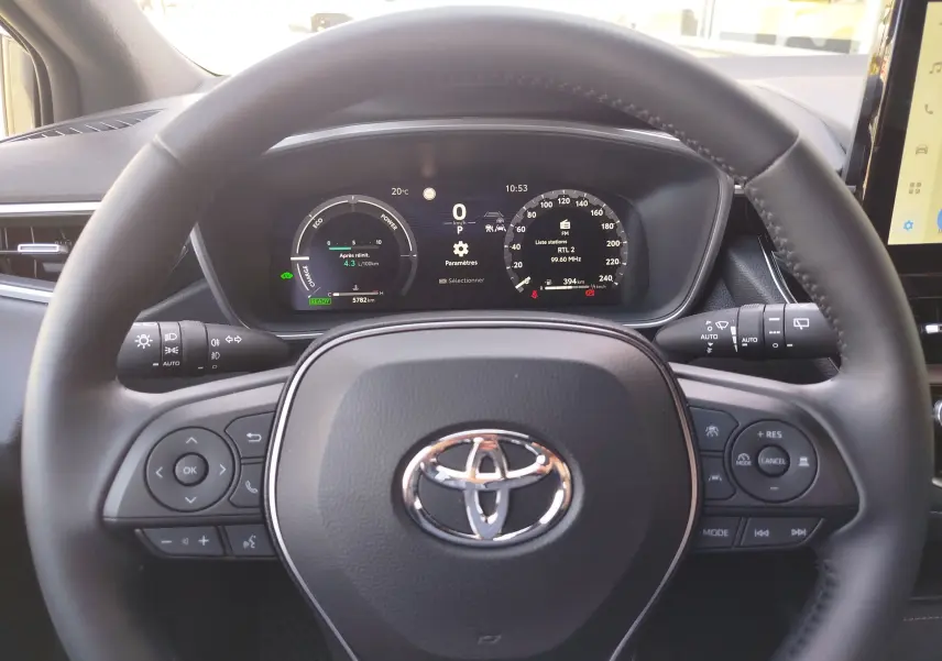 Vue intérieure centrée sur le volant noir de la Toyota Corolla Touring Sport 2026 avec tableau de bord numérique allumé.