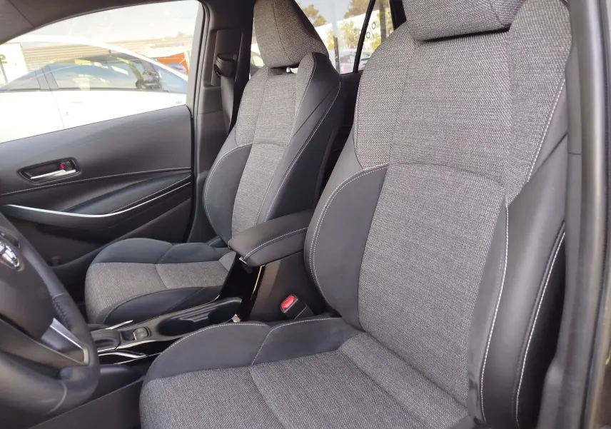 Vue intérieure côté conducteur de la Toyota Corolla Touring Sport 2026, sièges tissu gris et cuir noir avec surpiqûres blanches.