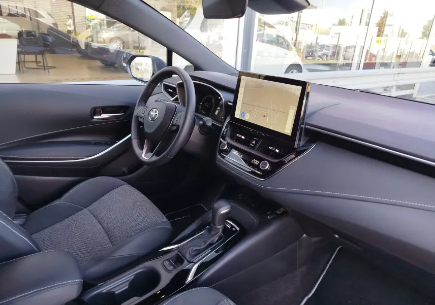 Vue intérieure côté conducteur de la Toyota Corolla Touring Sport 2026, avec écran tactile central et sellerie tissu gris.