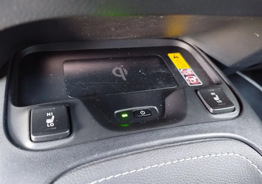 Gros plan sur la console centrale noire avec recharge sans fil et boutons de sièges chauffants de la Toyota Corolla Touring Sport.