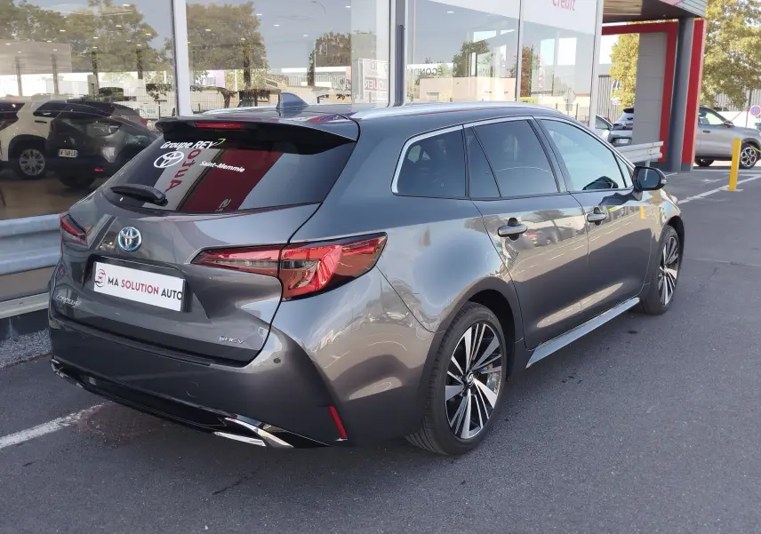 Vue 3/4 arrière droite d'une Toyota Corolla Touring Sport gris Atlas avec vitres teintées et jantes alliage bicolores.
