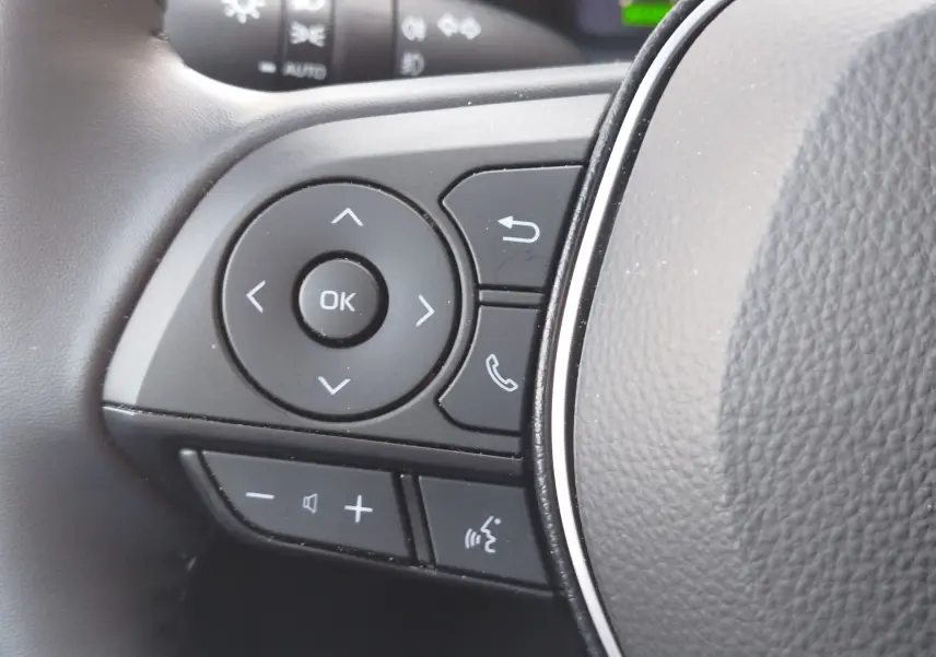 Gros plan sur les commandes multifonctions noires à gauche du volant en cuir gris d'une Toyota Corolla Touring Sport 2026.