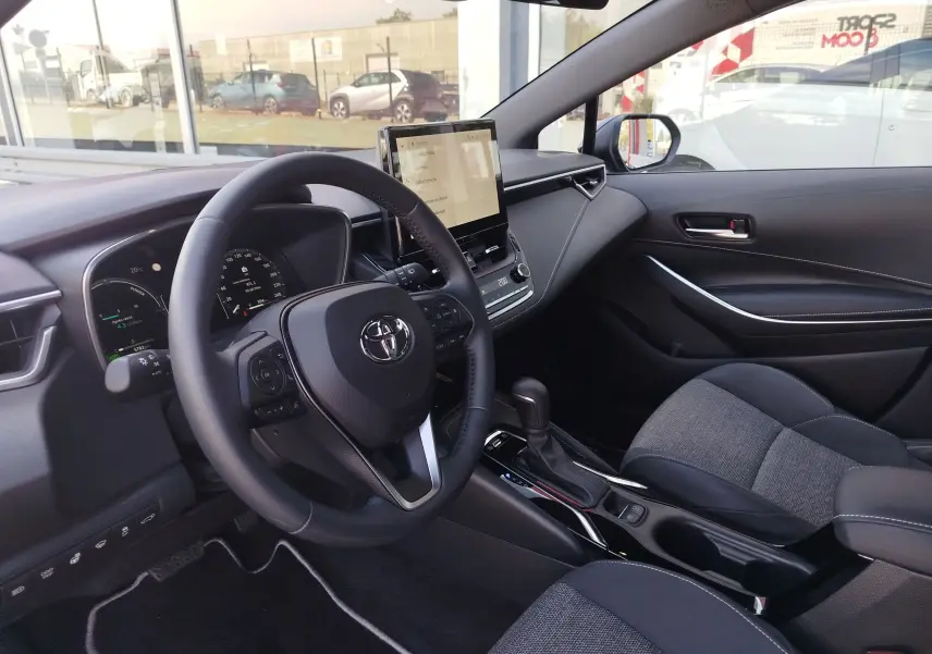 Intérieur de la Toyota Corolla Touring Sport 2026, vue côté conducteur, tableau de bord moderne avec écran tactile central.