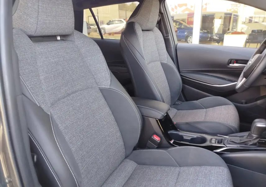 Vue intérieure côté droit montrant les sièges avant bi-matière tissu gris et cuir noir de la Toyota Corolla Touring Sport 2026.