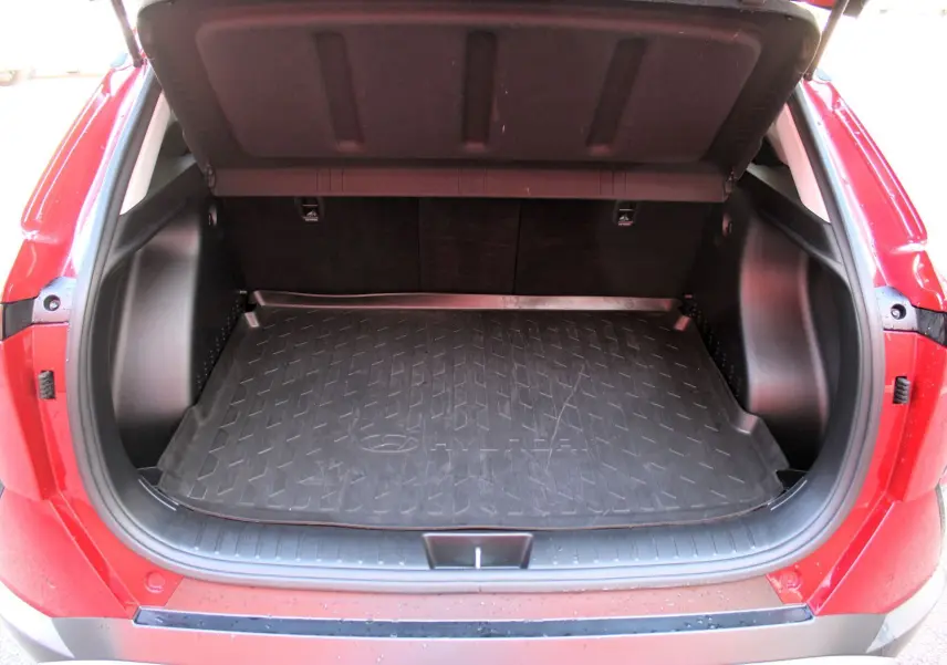 Coffre ouvert vu de l'arrière d'un Hyundai Kona 2024 rouge Ultimate Metal avec tapis de coffre noir.