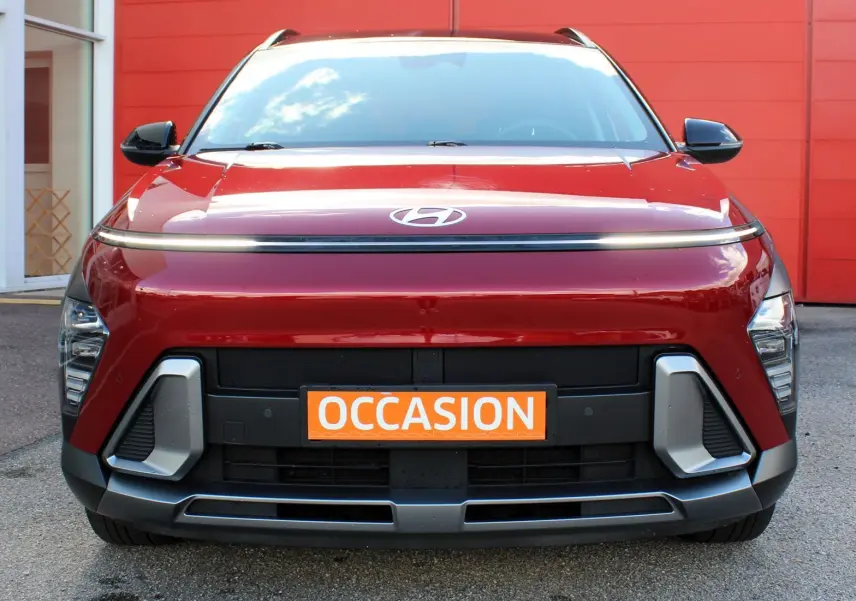 Vue avant d’un Hyundai Kona 2024 rouge Ultimate Metal avec détails noirs et plaque orange « Occasion » visible.