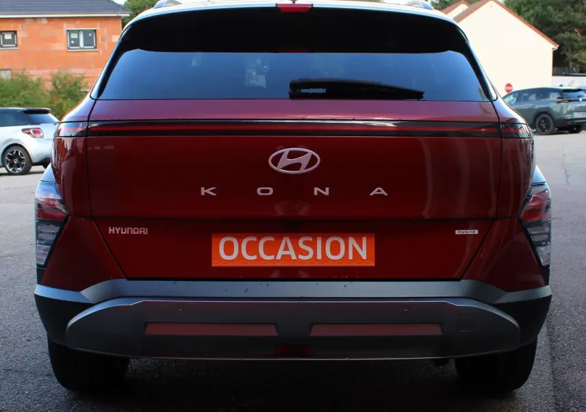 Vue arrière d'un Hyundai Kona 2024 rouge Ultimate Metal avec toit noir, badge hybride et plaque occasion.