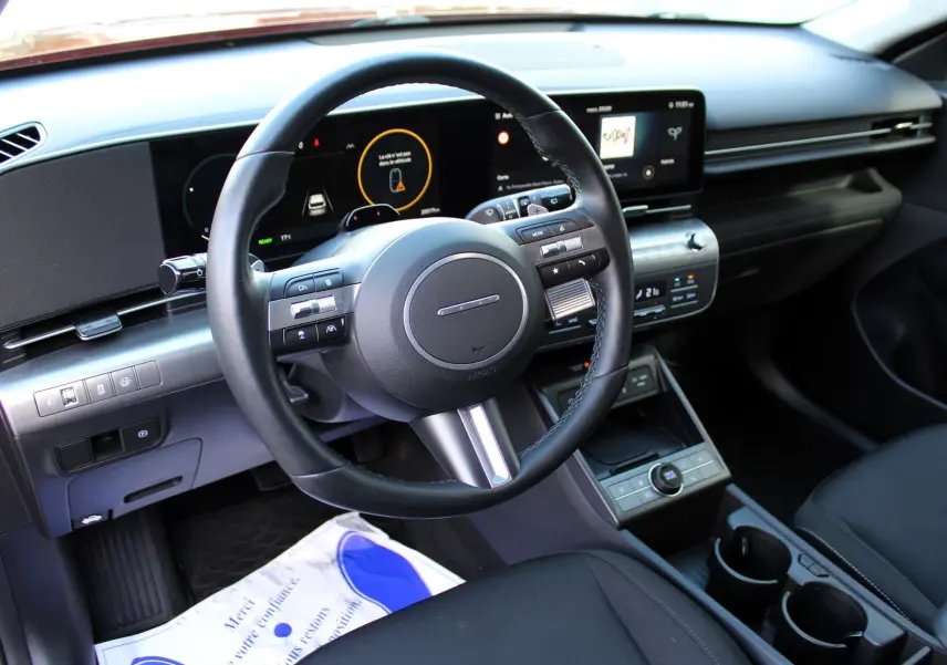 Vue intérieure du tableau de bord et volant du Hyundai Kona 2024 avec écran digital large et finition noire moderne.