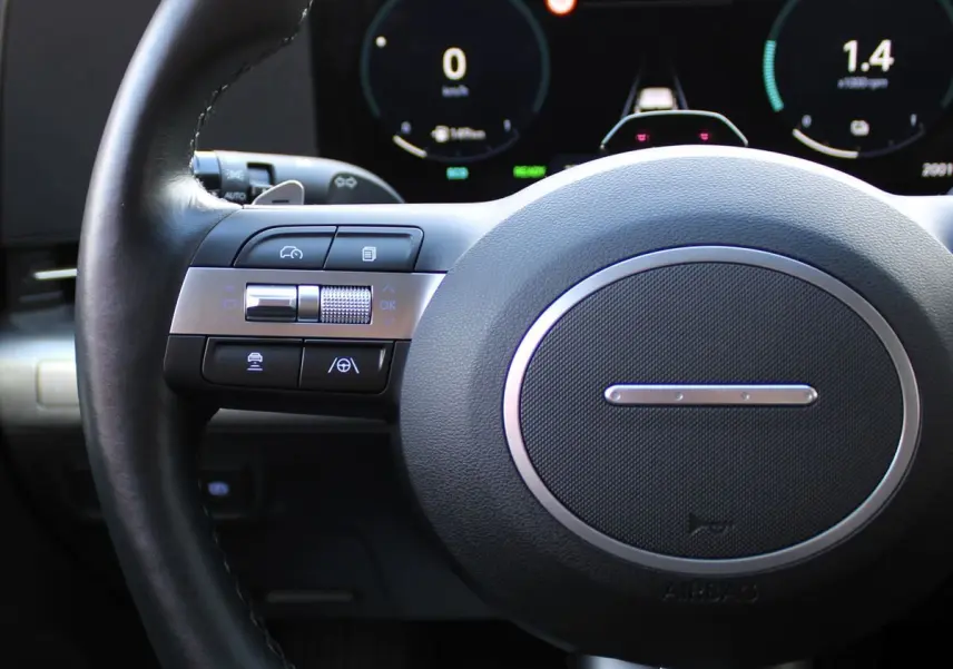 Gros plan sur le volant noir et les commandes multifonctions du Hyundai Kona 2024 avec tableau de bord numérique en arrière-plan.