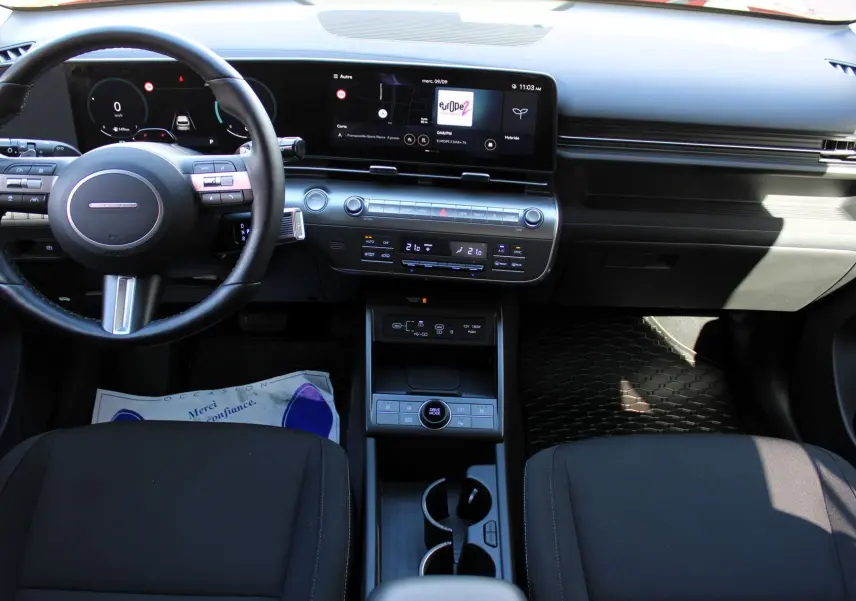 Vue intérieure avant du tableau de bord et console centrale noire du Hyundai Kona 2024 hybride avec écran tactile large et volant multifonction.