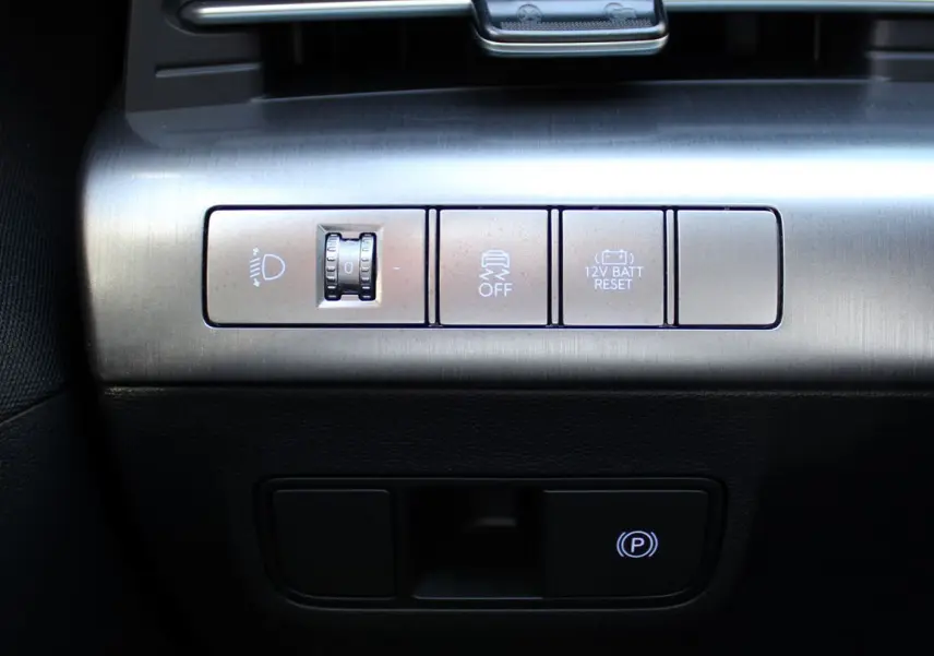 Gros plan sur les commandes argentées du tableau de bord du Hyundai Kona 2024, avec bouton frein à main électronique éclairé.