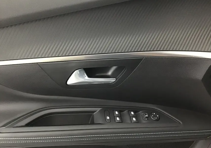 Gros plan sur la garniture intérieure de la porte côté gauche du Peugeot 5008 blanc nacré, avec commandes des vitres et poignée argentée.