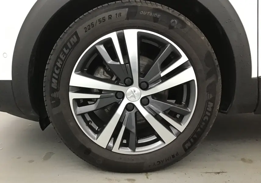 Gros plan sur la roue avant gauche du Peugeot 5008 blanc nacré, jante alliage 18 pouces au design moderne.
