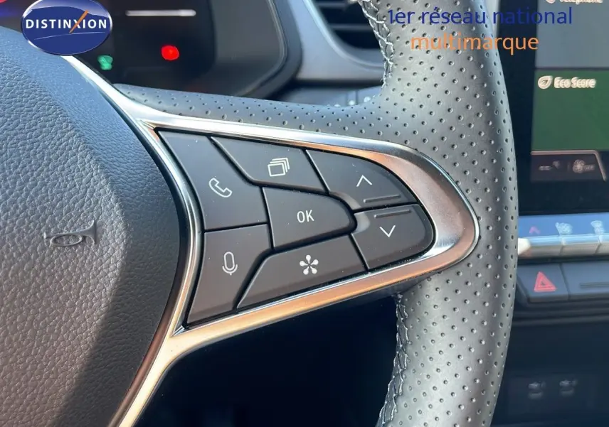 Gros plan sur les commandes au volant en cuir perforé du Renault Captur blanc nacré 2025, avec écran tactile en arrière-plan.