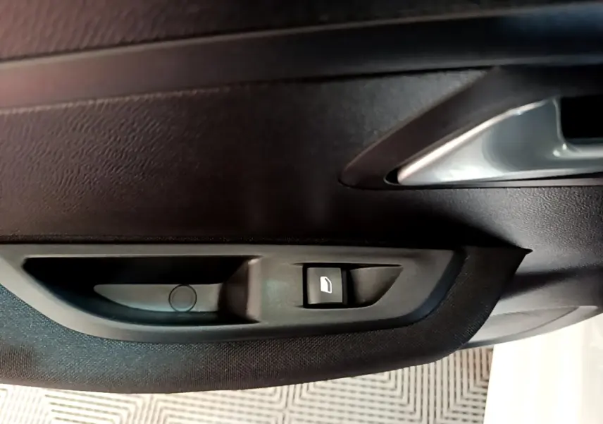 Gros plan sur la poignée intérieure et le bouton de lève-vitre côté conducteur d’une Peugeot 208 électrique blanche.