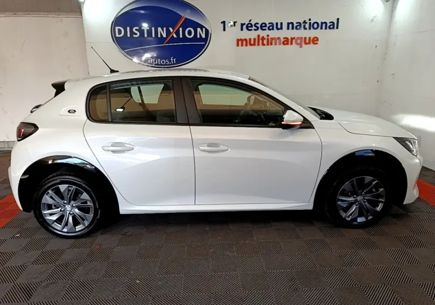 Vue de profil côté gauche d’une Peugeot 208 Electrique Active Business blanche en intérieur, avec jantes alliage et rétroviseurs blancs.