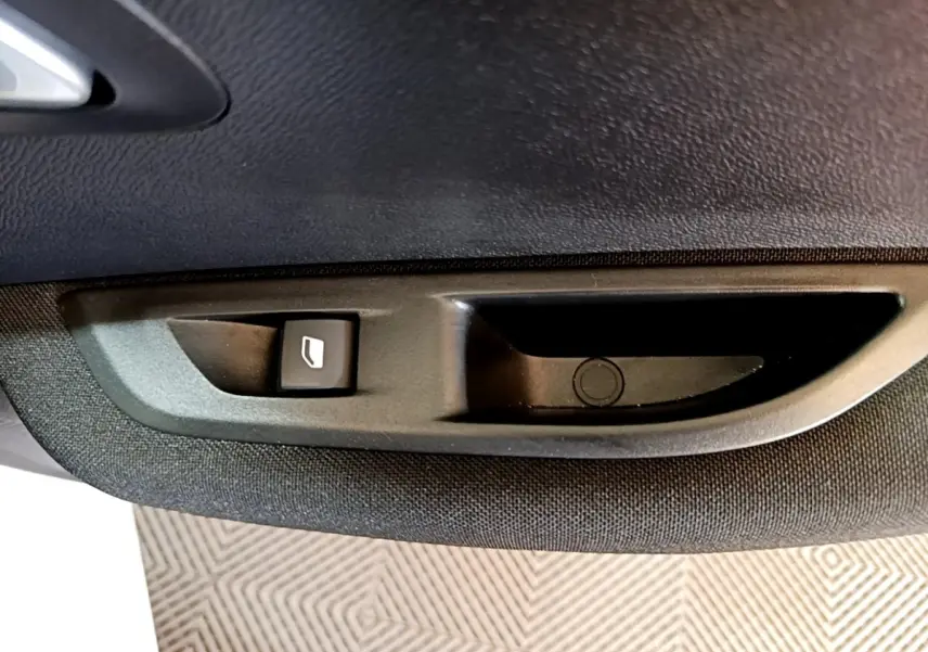 Gros plan sur le bouton de commande de lève-vitre côté gauche intérieur d’une Peugeot 208 électrique blanche.