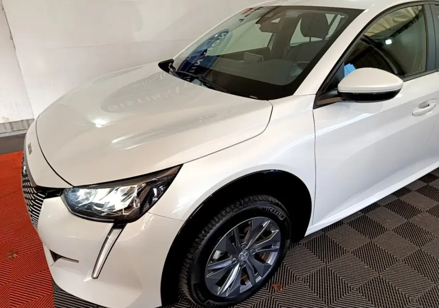 Vue 3/4 avant droite d'une Peugeot 208 électrique Active Business blanche avec phares LED et jantes alliage gris foncé.