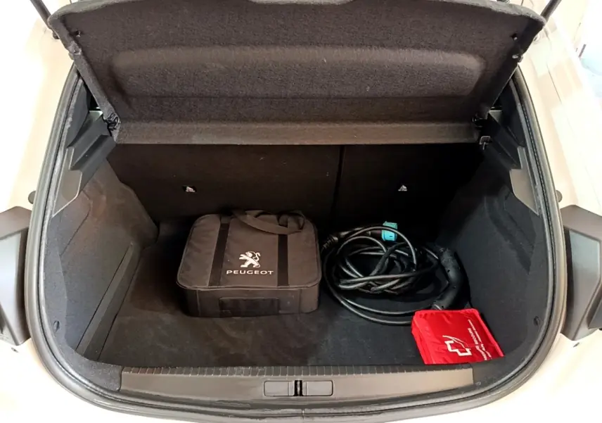 Vue plongeante sur le coffre ouvert blanc d'une Peugeot 208 électrique avec câble de recharge et sacoche Peugeot noire.