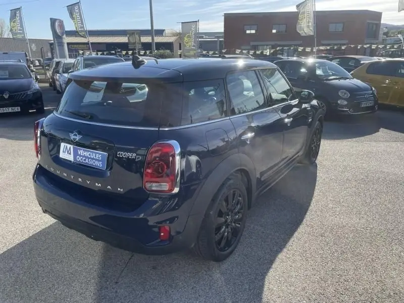 Vue 3/4 arrière droite d'une MINI Countryman Cooper D bleu foncé avec jantes noires, stationnée en extérieur sur un parking.
