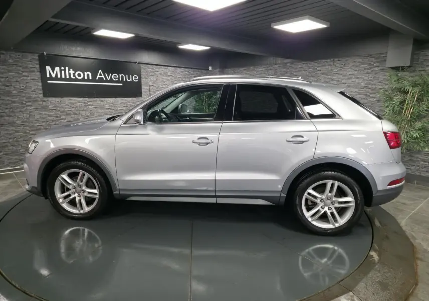 Audi Q3 gris métallisé vue de profil côté gauche dans un showroom avec jantes en alliage cinq branches.