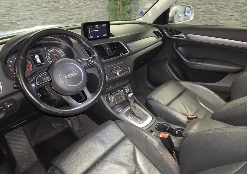 Vue intérieure côté conducteur de l'Audi Q3 2016, sellerie cuir noir et tableau de bord avec écran central.