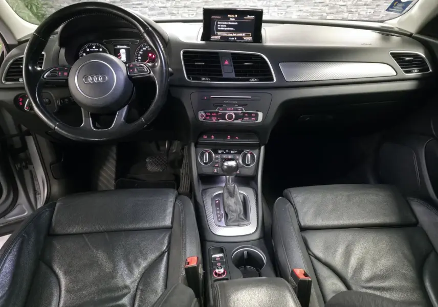 Vue intérieure avant de l'Audi Q3 1.4 TFSI 2016 avec sellerie cuir noire, console centrale et volant multifonction.