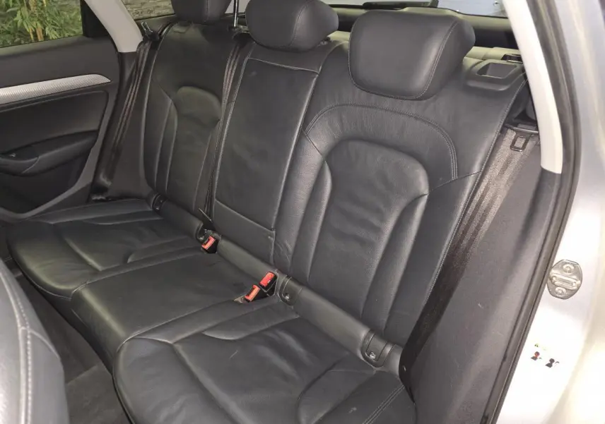Vue intérieure côté droit sur la banquette arrière en cuir noir de l'Audi Q3 gris 2016 avec ceintures de sécurité visibles.
