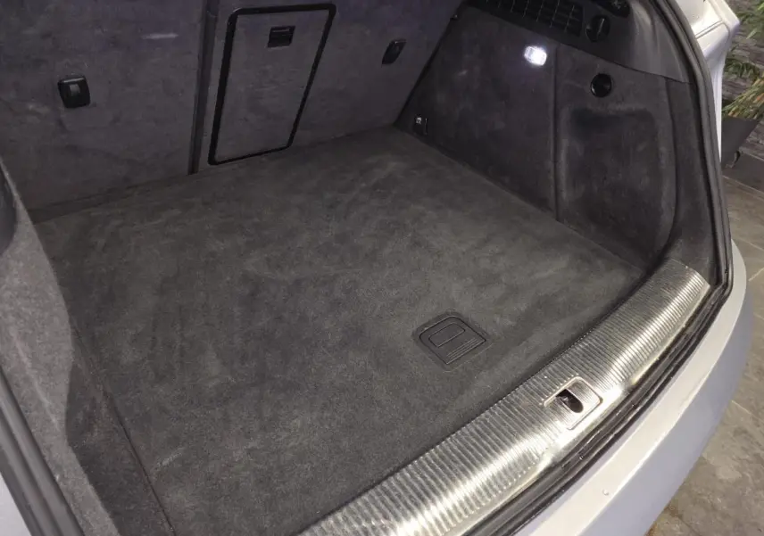 Vue du coffre ouvert de l'Audi Q3 gris, montrant la moquette noire et la garniture avec éclairage intérieur.