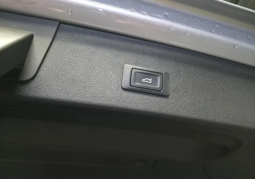 Bouton d'ouverture électrique du coffre sur la trappe intérieure d'un Audi Q3 gris, vue rapprochée.