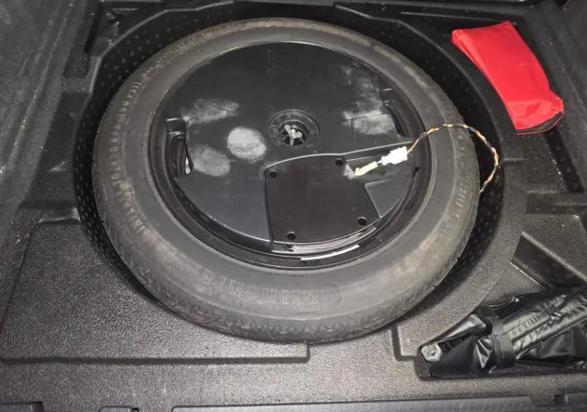 Vue rapprochée de la roue de secours noire dans le coffre d'un Audi Q3 gris, avec trousse de secours rouge à côté.