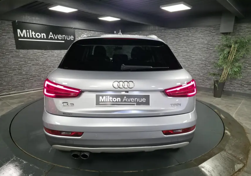 Vue arrière d'un Audi Q3 gris métallisé avec feux LED allumés et double sortie d'échappement visible.