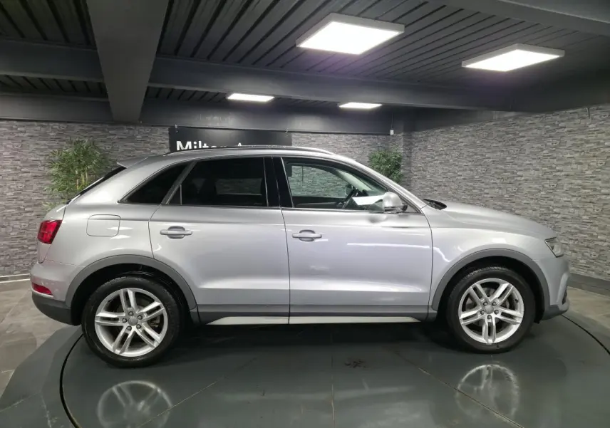 Audi Q3 gris métallisé vue de profil côté gauche dans un showroom avec jantes aluminium 5 branches doubles.