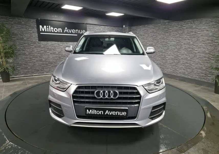 Audi Q3 gris métallisé vue de face, calandre Singleframe avec anneaux Audi et plaque Milton Avenue.