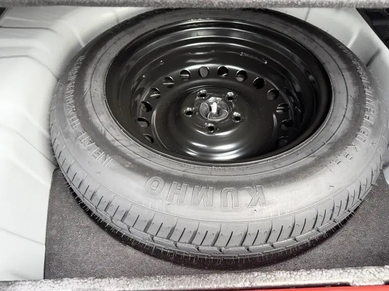 Pneu de secours noir monté sur jante acier, vu de dessus dans le coffre du Renault Arkana blanc 2025.