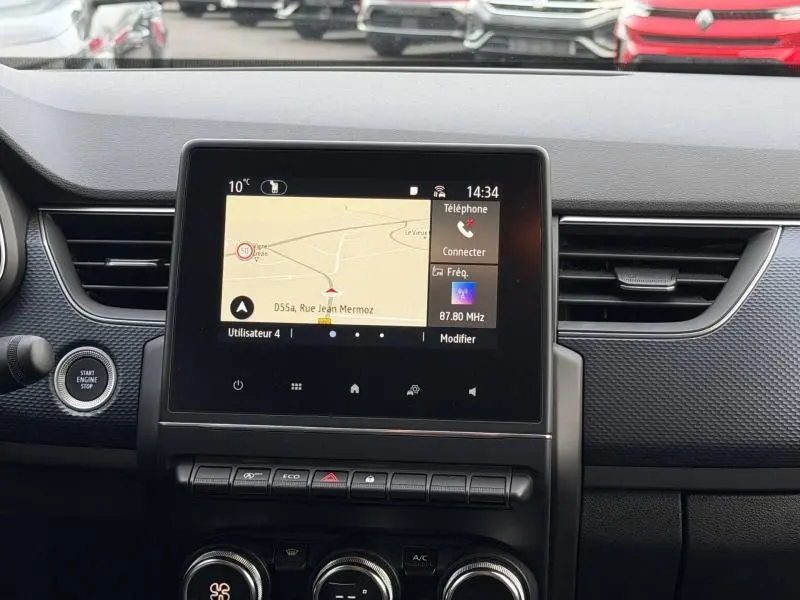 Vue rapprochée de l’écran tactile central du tableau de bord du Renault Arkana 2025 blanc, affichant la navigation et les commandes multimédia.