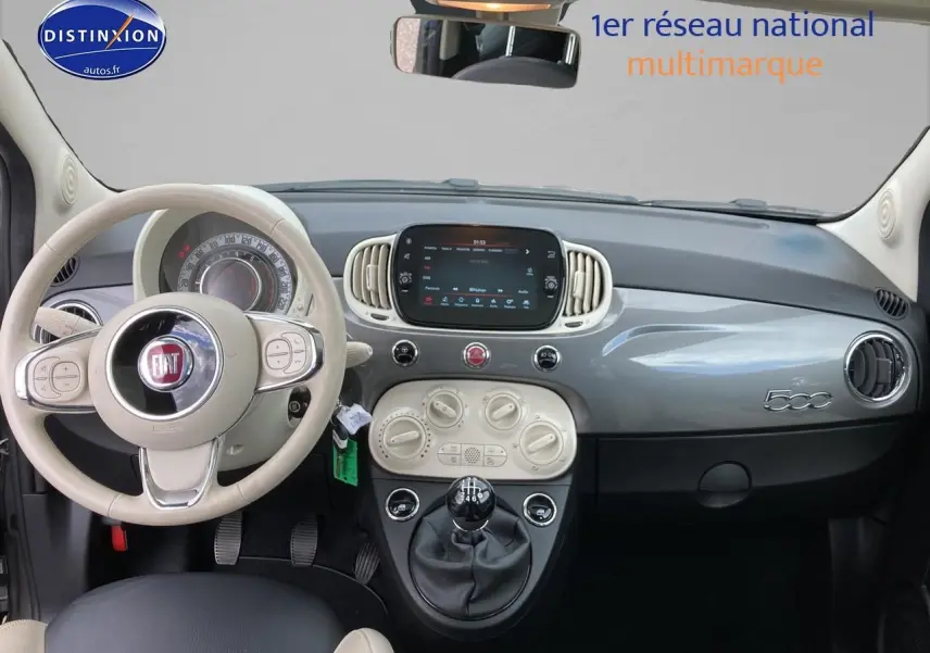 Vue intérieure frontale du tableau de bord gris et beige de la Fiat 500 1.0 70 bsg Dolcevita avec volant cuir et boîte manuelle.