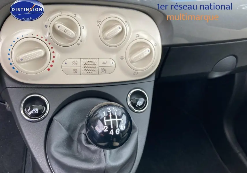 Gros plan sur la commande de boîte manuelle noire et les réglages de climatisation beige dans l’habitacle gris d’une Fiat 500.