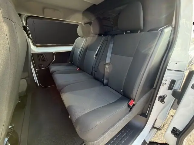 Vue intérieure côté droit du Citroën Jumpy XL blanc 2026, banquette arrière 3 places avec ceintures et cloison vitrée.
