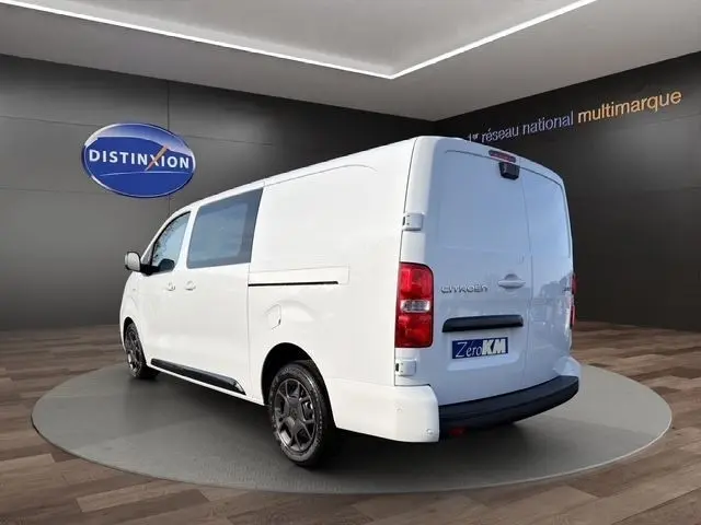 Vue 3/4 arrière droite d'un Citroën Jumpy XL blanc stationné en intérieur avec jantes noires et vitres teintées.