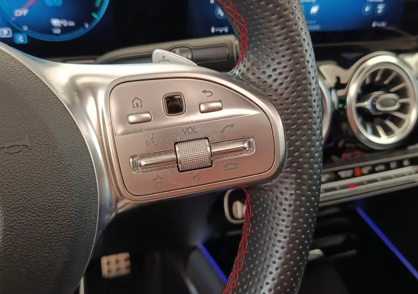Gros plan sur le volant cuir perforé avec surpiqûres rouges du Mercedes GLA 250 e AMG Line, commandes audio intégrées.