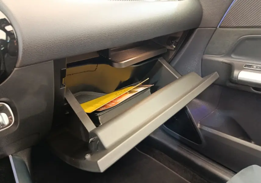 Gros plan sur la boîte à gants ouverte côté passager du Mercedes GLA 250 e AMG Line noir, intérieur sombre.