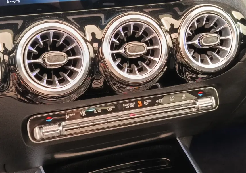 Détail intérieur du tableau de bord noir du Mercedes GLA 250 e AMG Line 2021, avec trois aérateurs ronds chromés et commandes climatisation.